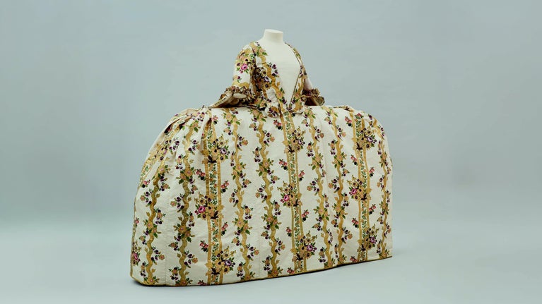 A very wide 18th century dress made from cream silk brocade with a luxurious design of tumbling floral bouquets against stripes and meanders of gold thread.